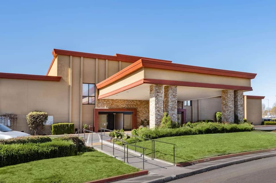 Modern institutional building exterior with cream and rust-colored panels, stone columns, and manicured lawn