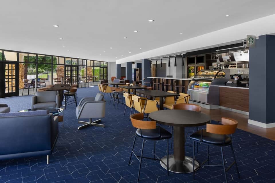 Modern hotel lobby and café with blue seating, wooden tables, coffee counter, and large windows