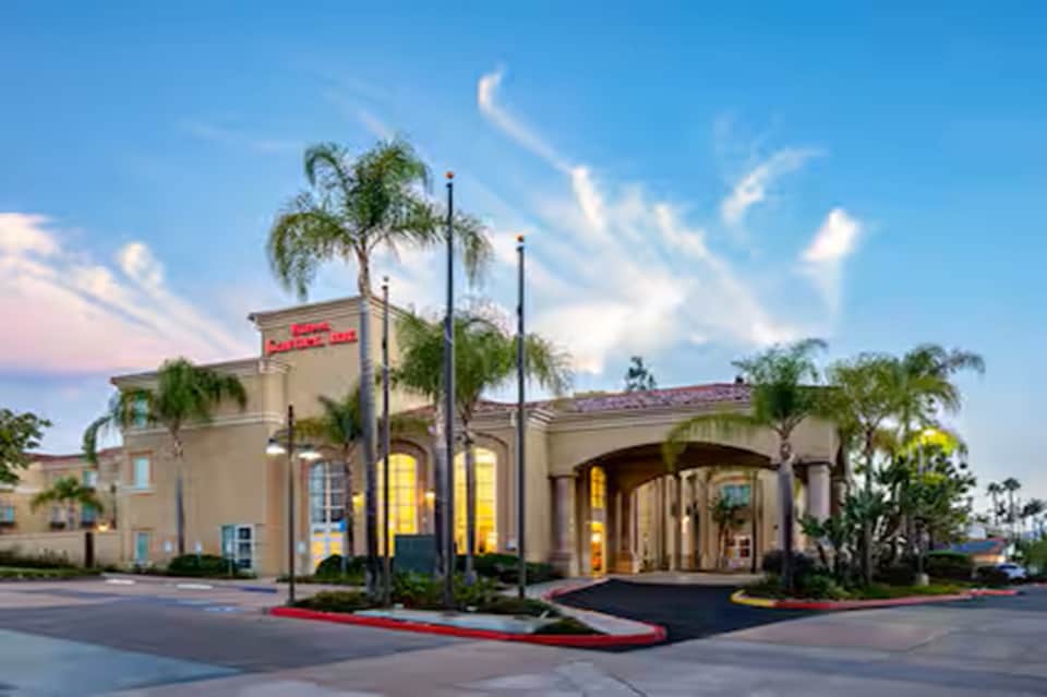 Modern resort entrance at dusk with palm trees, illuminated archway, and manicured grounds