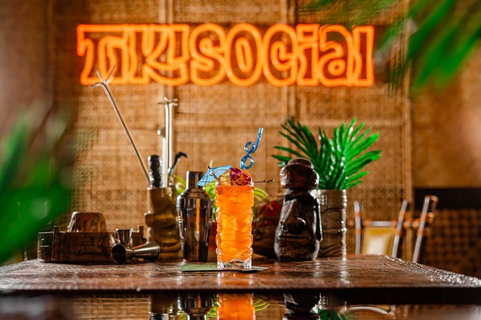 Cocktail bar counter with orange neon sign and tropical drink in highball glass