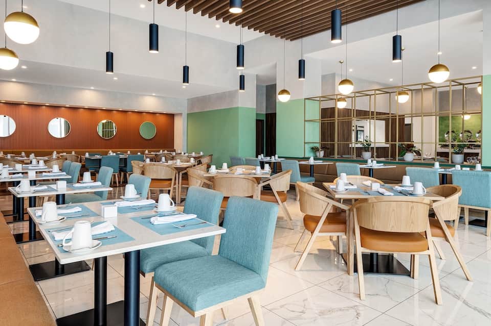 Contemporary restaurant dining room with orange and green accent walls, wooden furniture, pendant lights