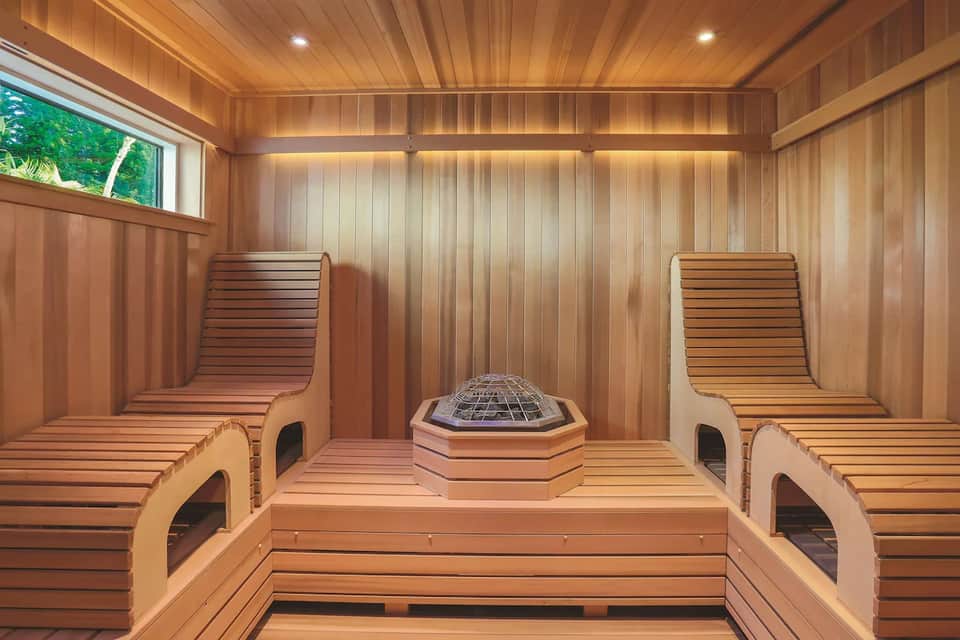 Wooden sauna interior with benches, hexagonal heater, and window overlooking green vegetation