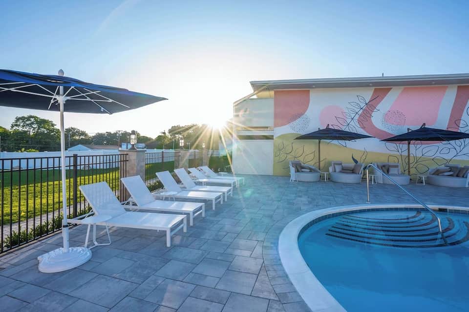 Spa pool area with artistic mural wall, white loungers, umbrellas, and waterfront views at golden hour