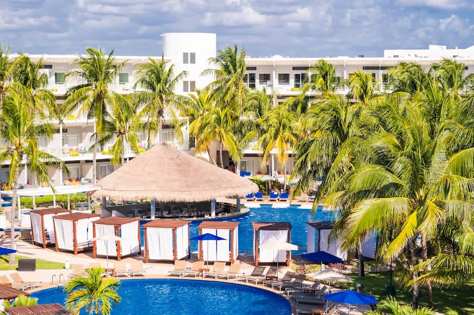 Resort pool with thatched umbrella, white cabanas, and modern white buildings