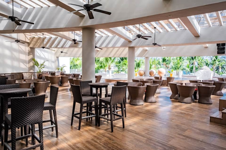 Spacious covered lounge area with rattan furniture, high ceilings, fans, and tropical views