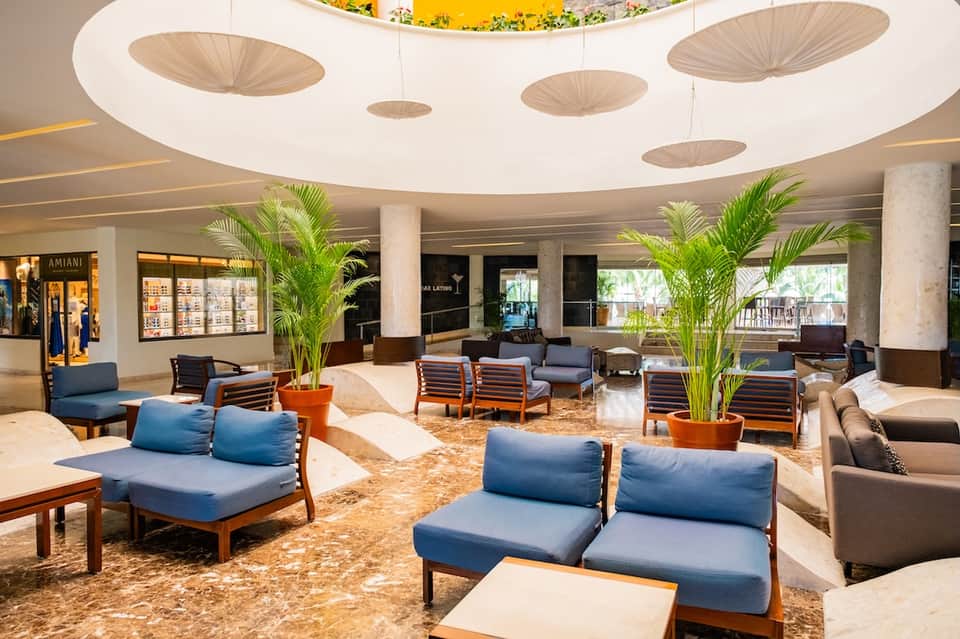 Hotel lobby with curved ceiling, decorative disc elements, potted palm plants, and modern seating