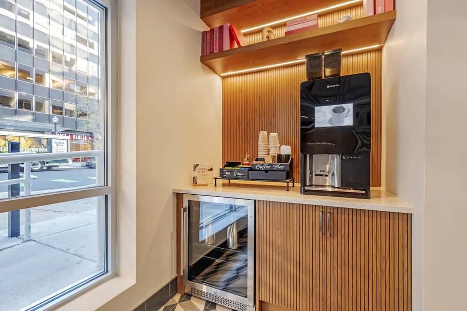 Modern coffee bar with espresso machine, shelving, and warm wood finishes in urban hotel lobby