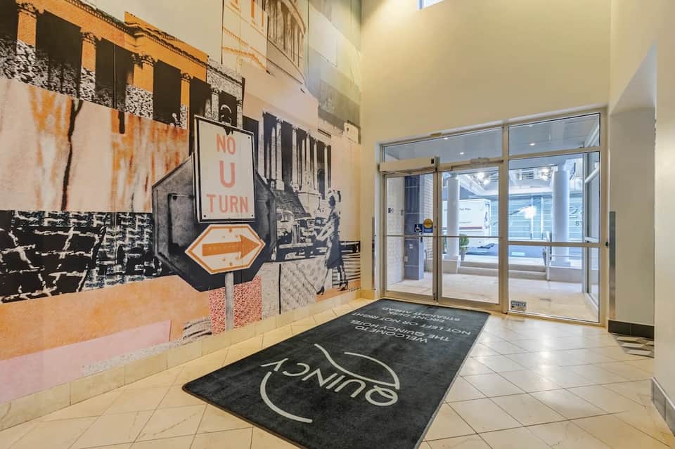 Hotel lobby entrance with artistic wall mural, glass doors, and light wood flooring with branded mat
