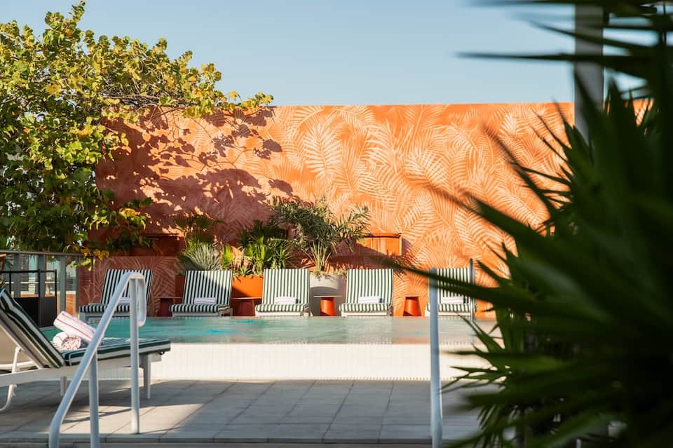 Modern pool deck with orange patterned wall, lounge chairs, and shallow swimming pool