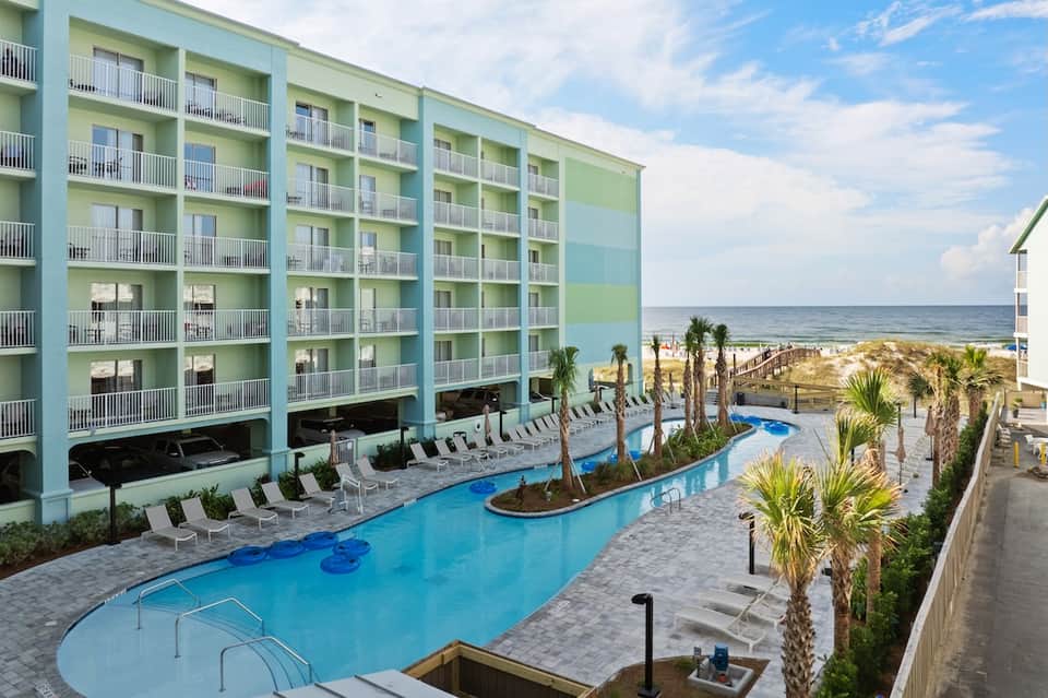 Beachfront resort with turquoise pool, palm trees, and ocean view from balcony