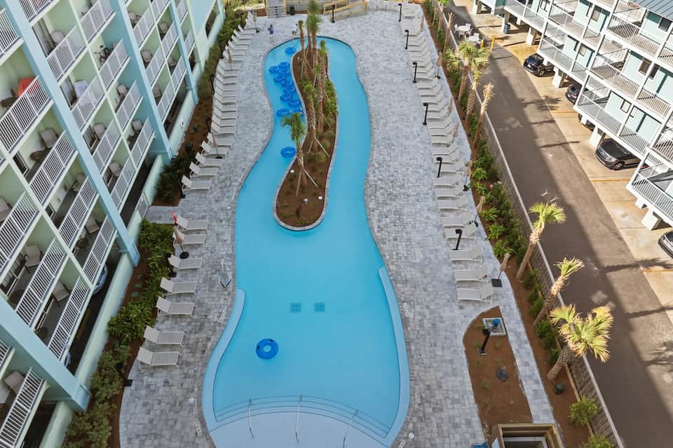 Aerial view of curved swimming pool with palm trees between residential buildings