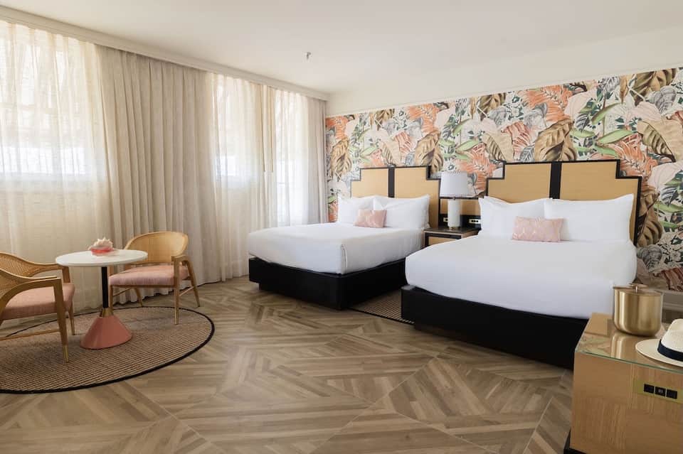 Hotel bedroom with two queen beds, botanical wallpaper accent wall, and modern contemporary decor in warm tones