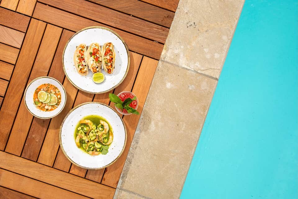 Gourmet dishes on wooden deck overlooking bright turquoise swimming pool