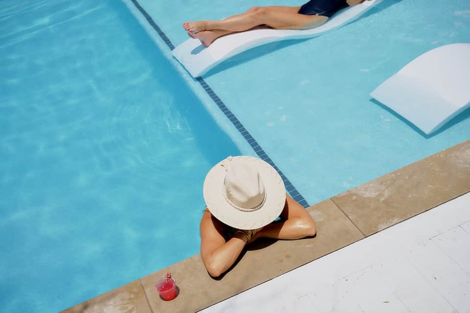 Woman in white hat relaxing on lounge float in crystal blue pool