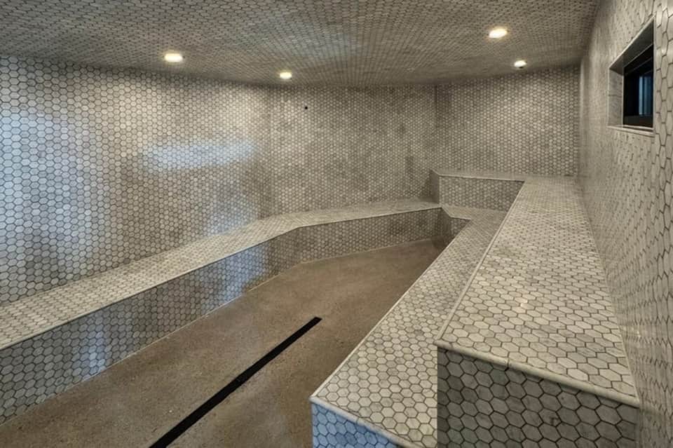 Contemporary steam room with hexagonal tile walls, wooden bench seating, and recessed lighting