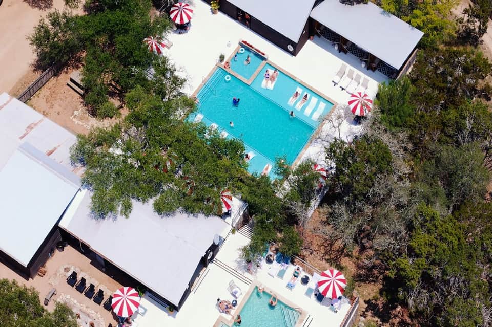 Aerial view of resort pools, umbrellas, loungers, and manicured grounds surrounded by vegetation