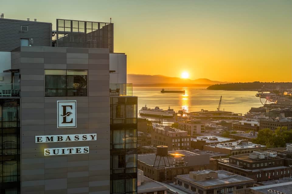 Embassy Suites hotel exterior at sunset overlooking waterfront and city buildings