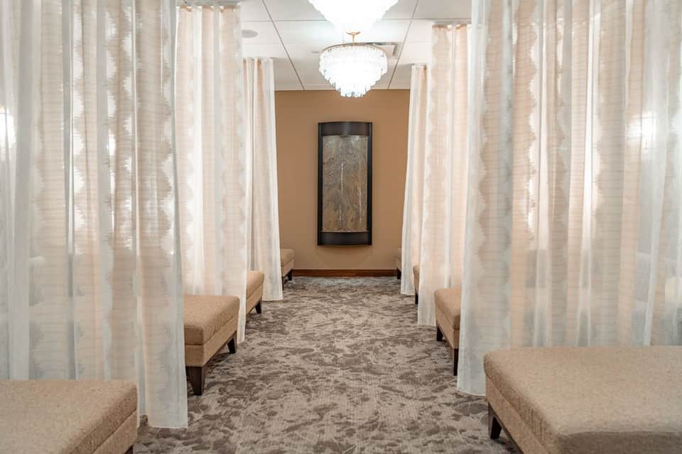 Spa hallway with sheer white curtains, beige seating alcoves, elegant lighting, and artwork