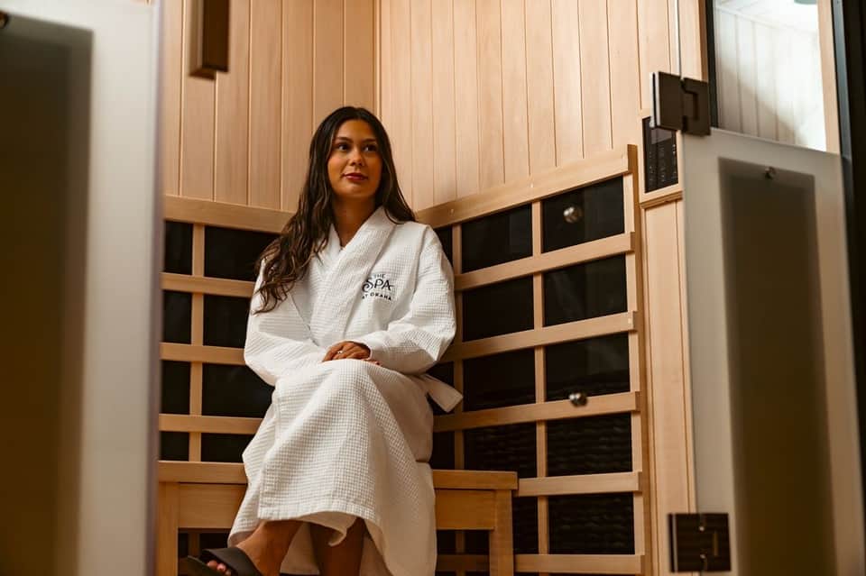 Woman in spa robe standing in modern sauna facility with wooden doors