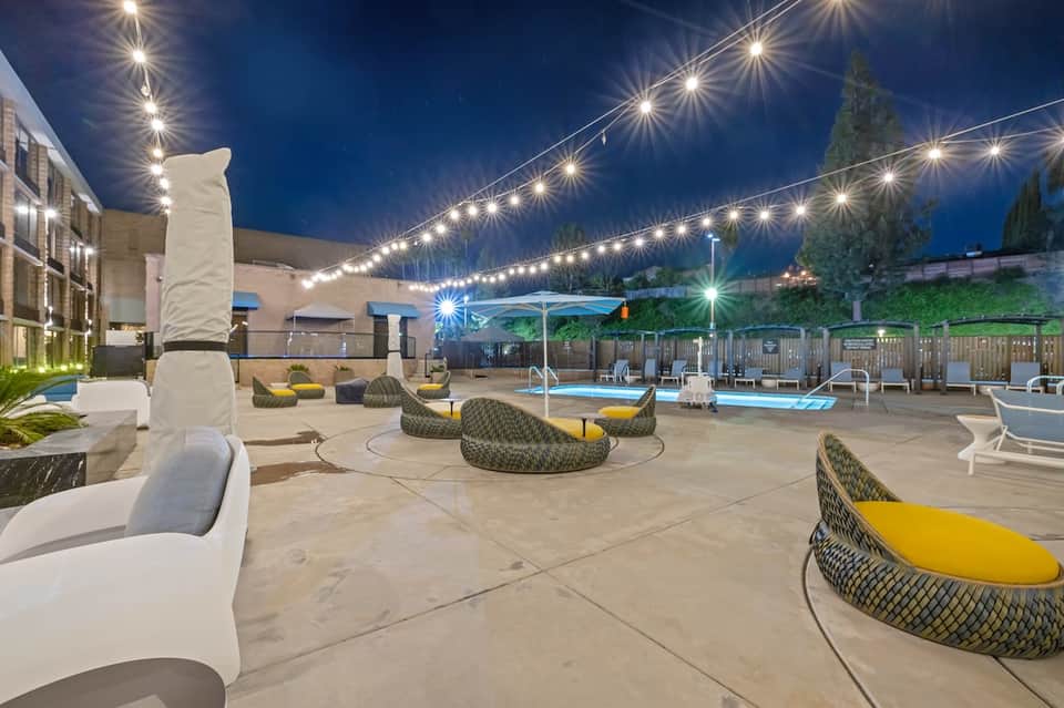 Modern rooftop pool deck at night with string lights, lounge chairs, and city views