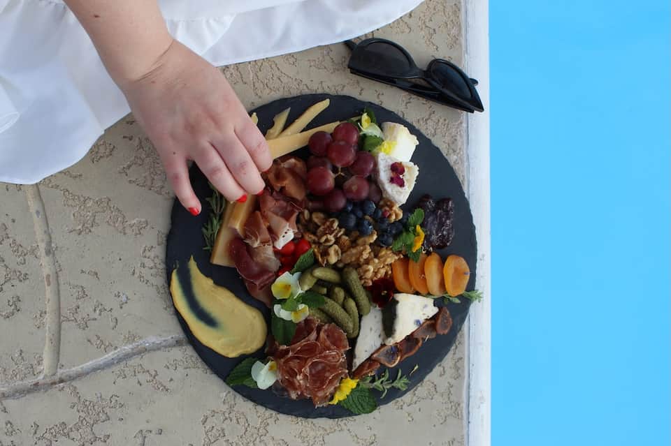 Gourmet charcuterie board with fruits, meats, cheeses, and flowers on a stone ledge