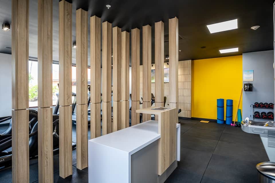 Modern gym facility with wooden dividers, yellow accent wall, and fitness equipment