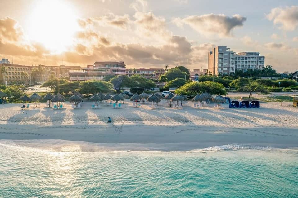 Beachfront resort at sunset with tiki umbrellas, lounge chairs, and buildings along the shoreline