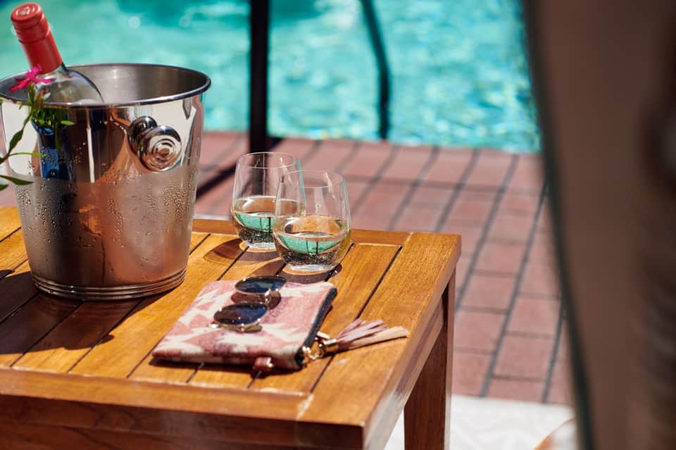 Poolside wine service with ice bucket, glasses, and charcuterie on wooden table