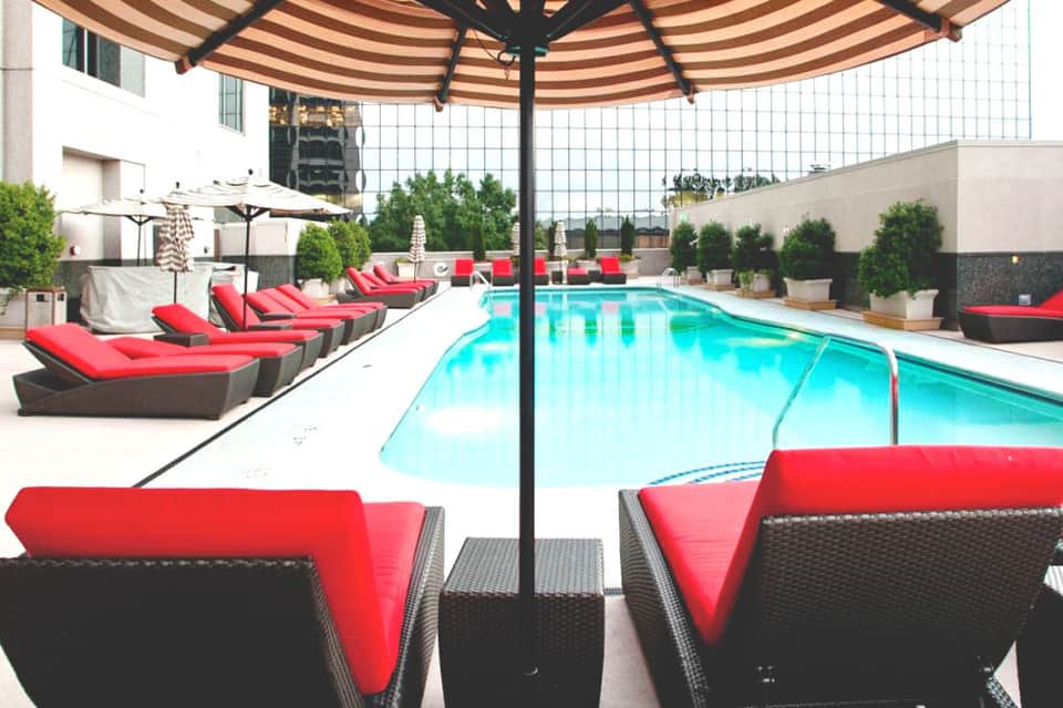 Luxury rooftop pool area with bright turquoise water, red lounge chairs, and black umbrellas