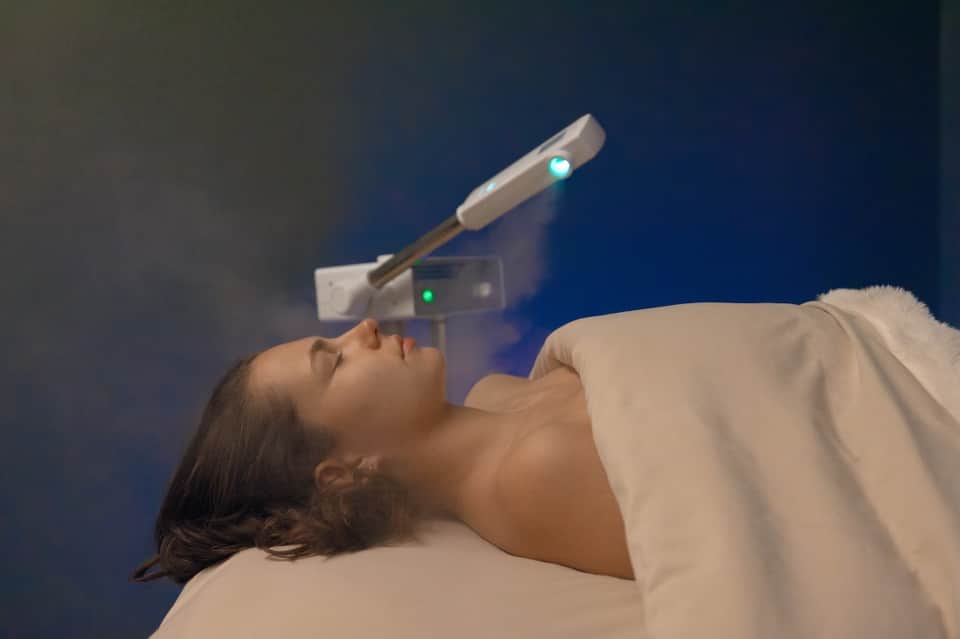 Woman receiving spa facial treatment with advanced handheld beauty device against blue background