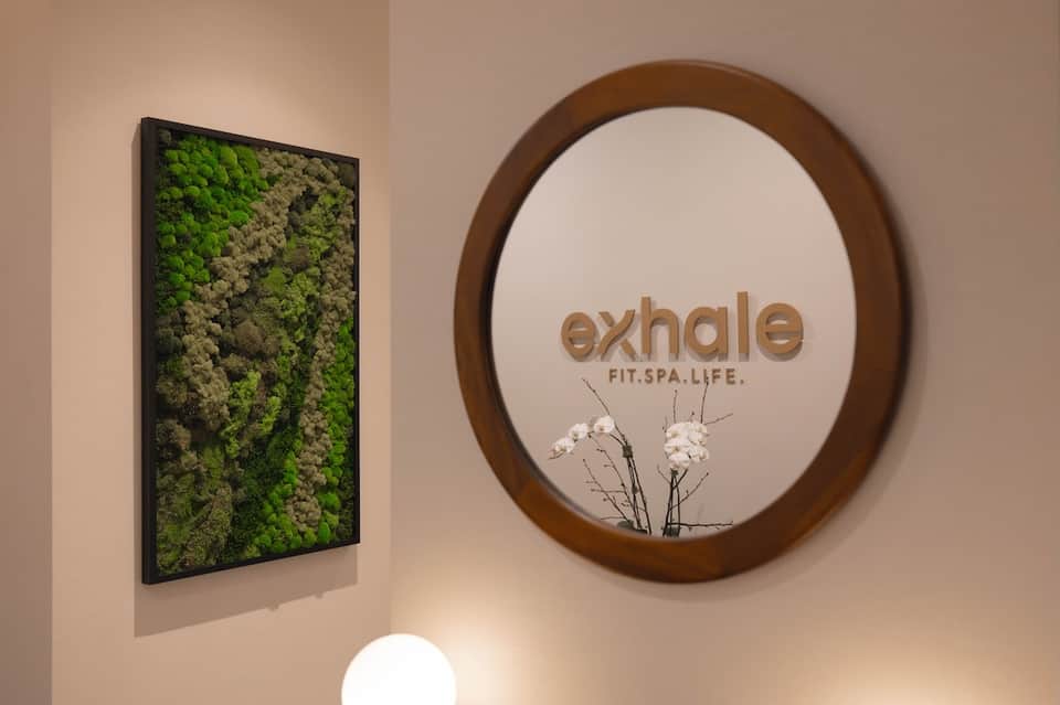 Spa entrance signage reading 'exhale FIT.SPA.LIFE' with moss wall art and minimalist wellness branding