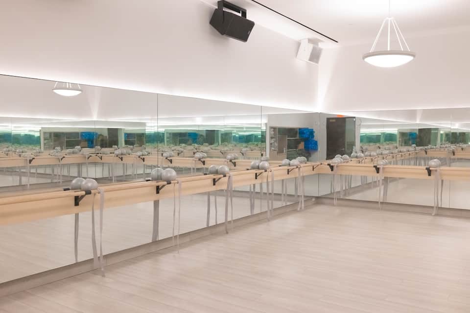 Indoor dance studio with mirrors, ballet barres, wooden floors, and natural lighting from windows