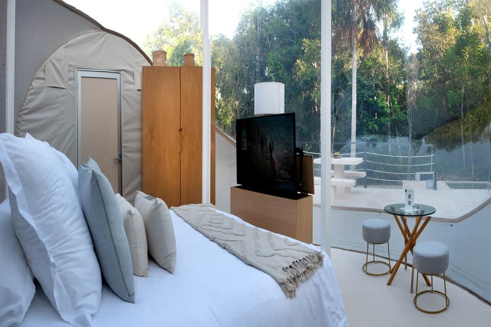 Modern hotel bedroom with platform bed, glass wall access to terrace, TV, and minimalist furnishings