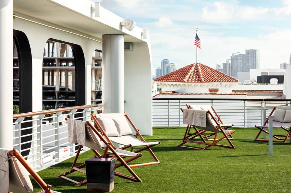 Rooftop terrace with deck chairs, green lawn, and city skyline view with American flag