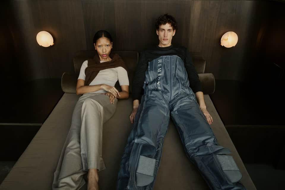 Two people sitting on modern gray bench in minimalist room with round wall lights