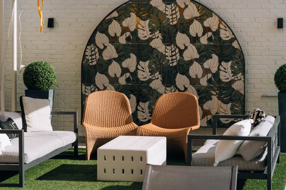 Outdoor lounge area with woven chairs, botanical backdrop, and modern patio seating