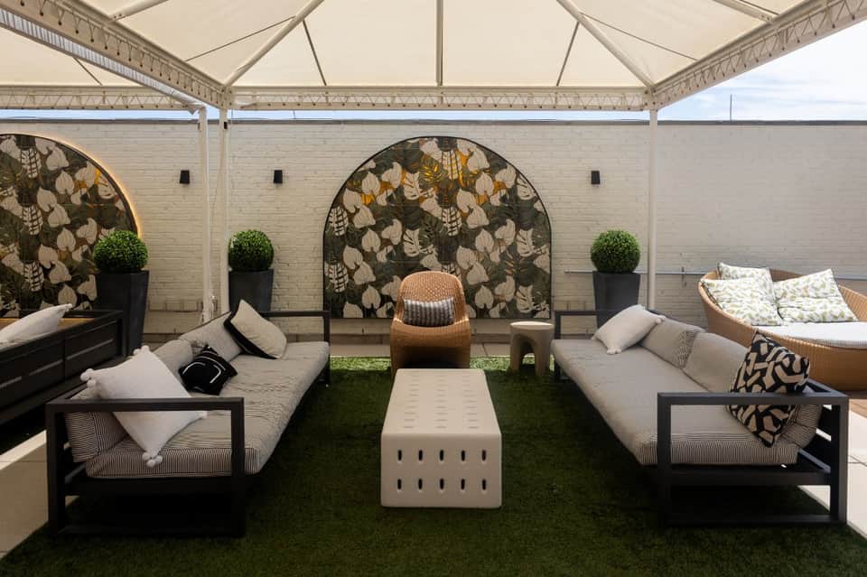 Rooftop lounge with white tent canopy, modular seating, decorative wall panels, and green turf