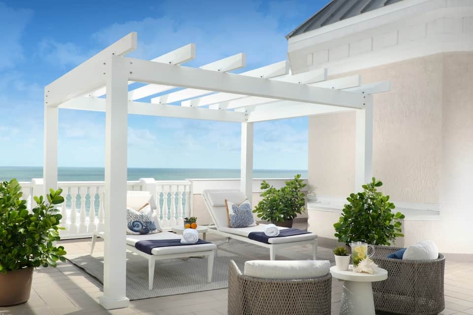 Beachfront pergola lounge with ocean view, loungers, and white wooden structure