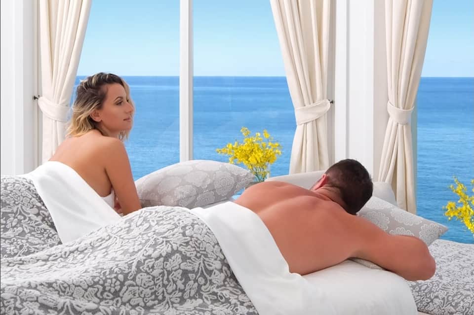 Couple relaxing on bed with ocean seascape view through large windows with flowing curtains