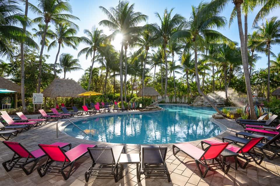 Resort pool surrounded by colorful lounge chairs, palm trees, and thatched umbrellas