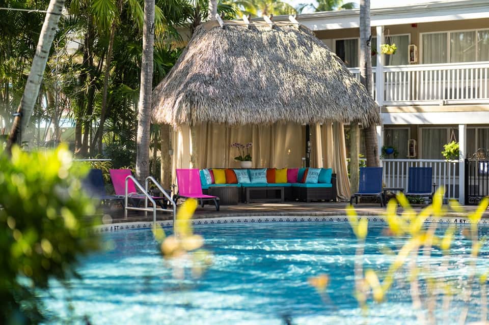 Thatched-roof poolside cabana with colorful cushions beside a resort pool and tropical landscaping