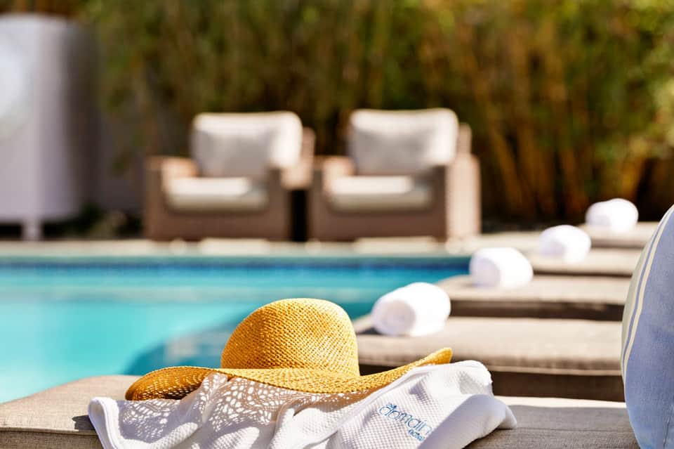 Yellow straw hat and towel on lounge chair by pool with cushioned seating in background