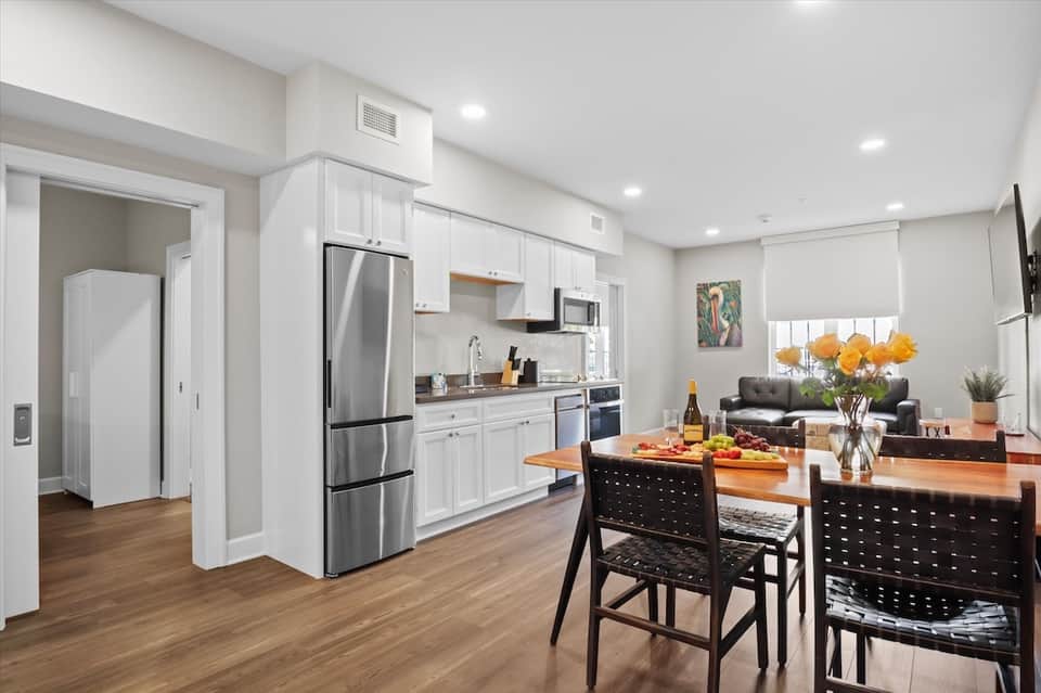 Bright modern apartment kitchen with white cabinetry, stainless steel appliances, and dining table
