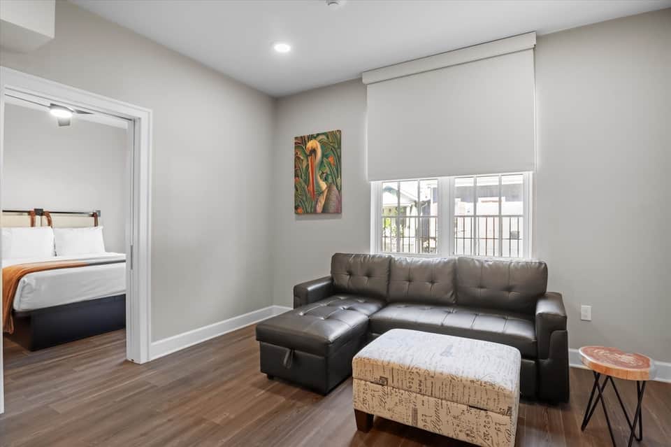 Modern resort bungalow interior with bedroom, black leather sofa, hardwood floors, and glass door