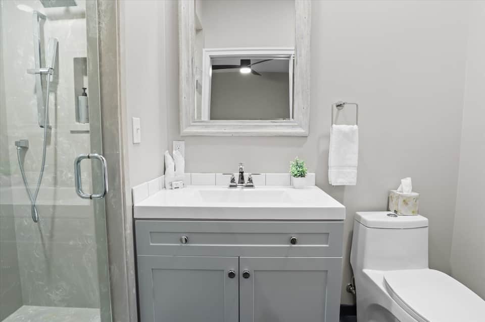 Clean modern bathroom with gray vanity, white sink, shower, and framed mirror