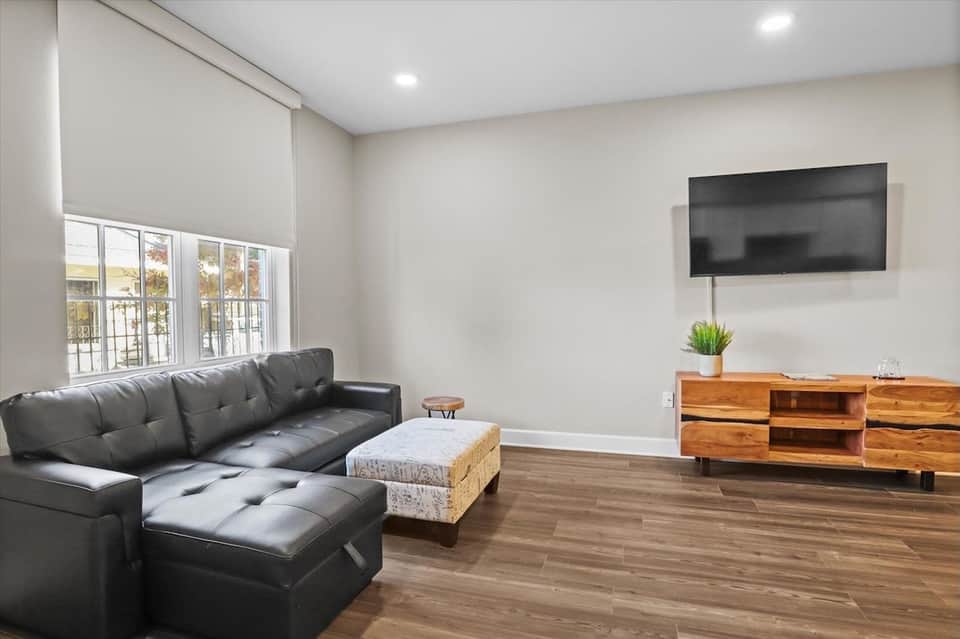 Contemporary living room with black leather sectional, wooden TV stand, and waterfront windows