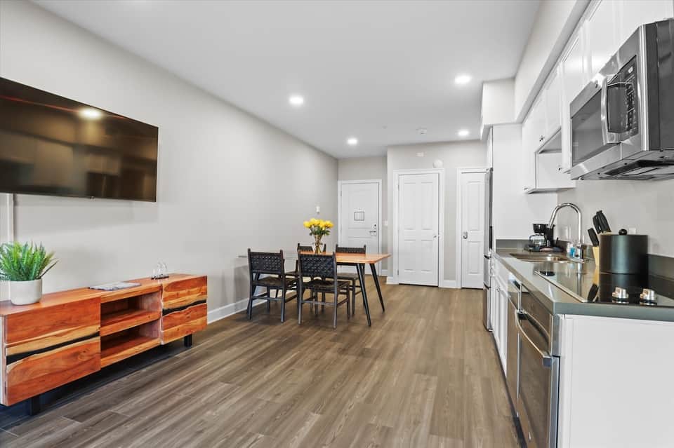 Modern apartment kitchen and dining area with white cabinets, stainless steel appliances, and wood flooring