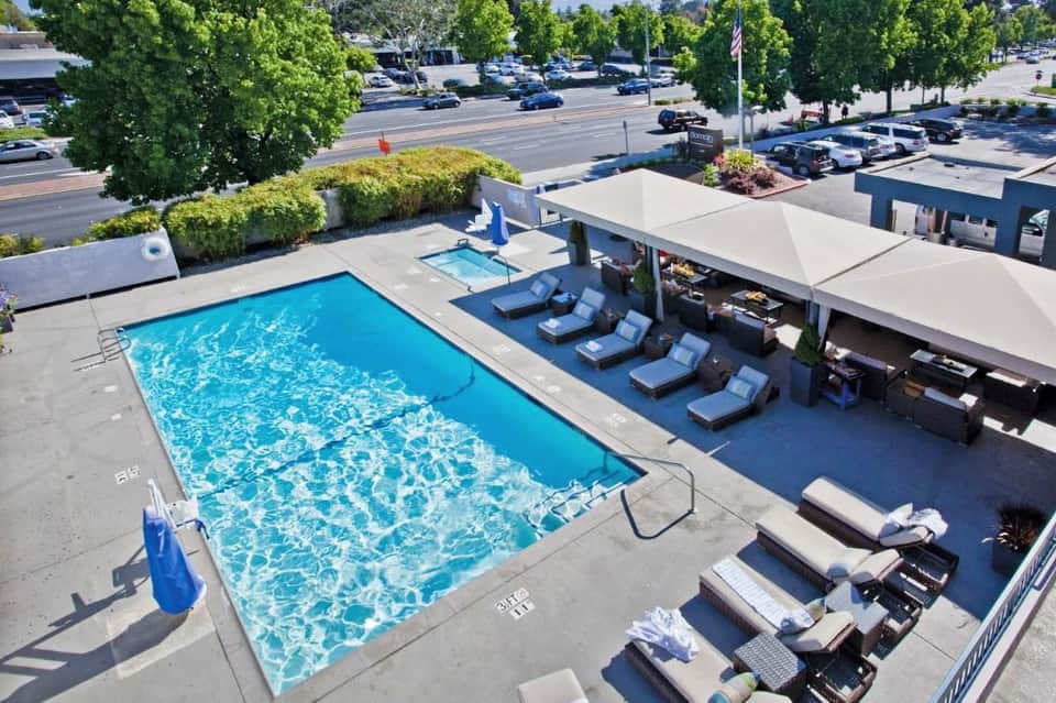 Aerial view of resort pool with lounge chairs, white umbrellas, and parking lot beyond
