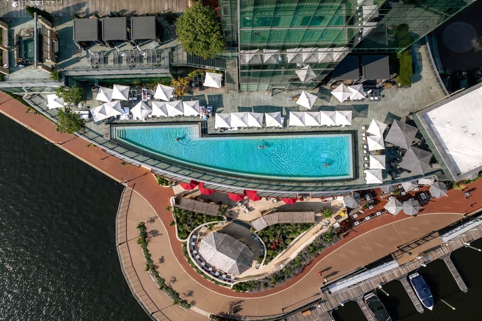 Aerial view of luxury resort with curved pool, white umbrellas, lounge chairs, and waterfront