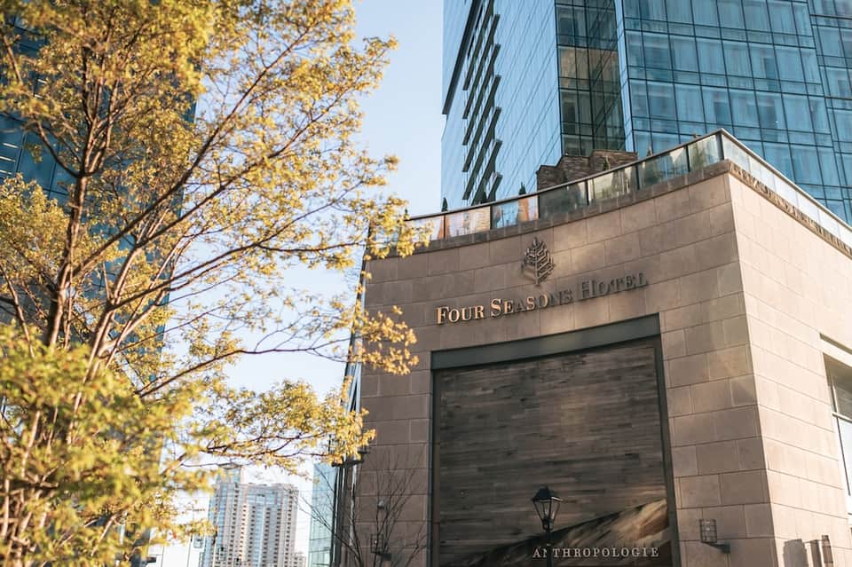Four Seasons Hotel entrance with stone facade, glass doors, and surrounding tall buildings